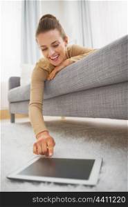 Happy young woman using tablet pc while laying on sofa