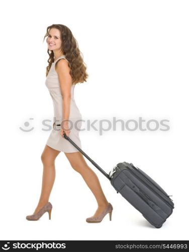 Happy young woman walking with wheels suitcase
