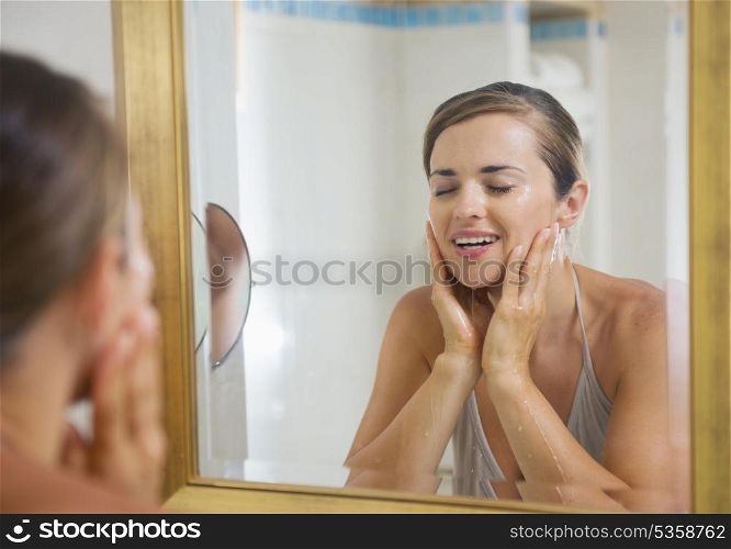 Happy young woman washing face in bathroom