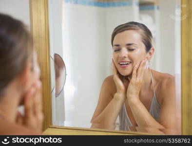 Happy young woman washing face in bathroom