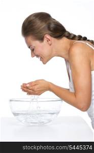 Happy young woman washing face in glass bowl with water