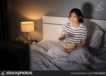 happy young woman watching TV on a bed at night