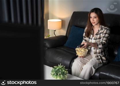 happy young woman watching TV on sofa at night
