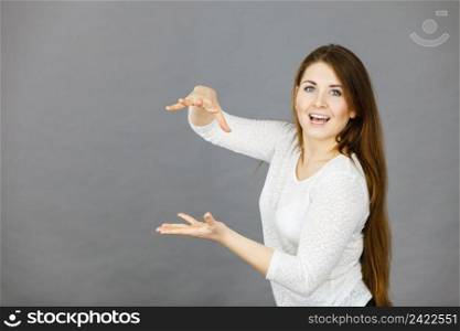 Happy young woman wearing white jumper blouse gesturing with hands presenting copyspace. Studio shot on grey background.. Happy woman presenting copyspace with hands