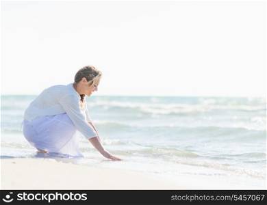 Happy young woman wetting hands in sea