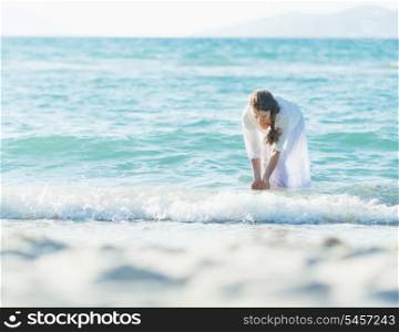 Happy young woman wetting hands in sea