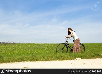 Happy young woman with a vintage bicycle on a green meadow