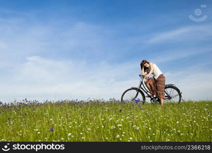 Happy young woman with a vintage bicycle on a green meadow