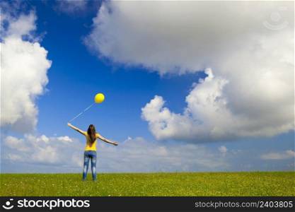 Happy young woman with a yellow balloon on a green meadow