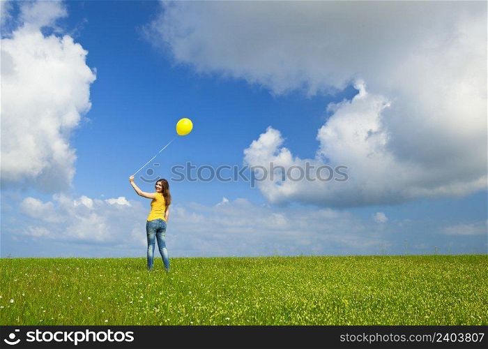 Happy young woman with a yellow balloon on a green meadow