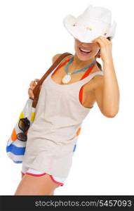 Happy young woman with beach bag hiding behind hat