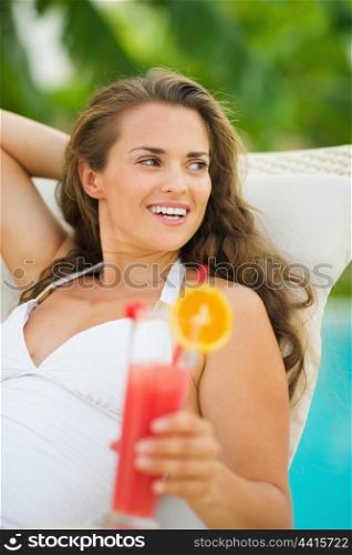 Happy young woman with cocktail laying on chaise-longue
