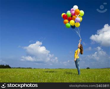 Happy young woman with colorful balloons on a green meadow