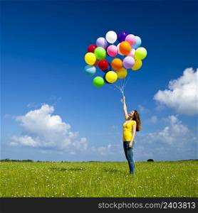 Happy young woman with colorful balloons on a green meadow