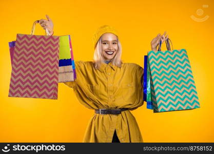 Happy young woman with colorful hair and paper bags after shopping isolated on yellow studio background. Seasonal sale, purchases, spending money on gifts concept.. Happy young woman with colorful hair and paper bags after shopping isolated