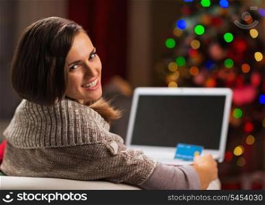 Happy young woman with credit card and laptop in front of Christmas tree