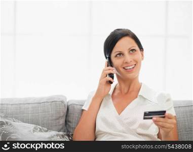 Happy young woman with credit card and speaking mobile phone
