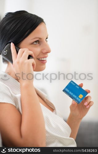 Happy young woman with credit card speaking mobile