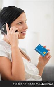 Happy young woman with credit card speaking mobile