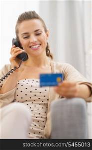 Happy young woman with credit card talking phone while sitting on sofa