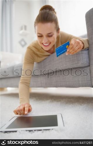 Happy young woman with credit card using tablet pc while laying on sofa