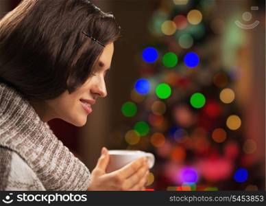 Happy young woman with cup of hot chocolate in front of christmas lights