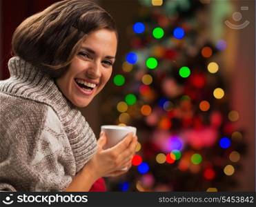 Happy young woman with cup of hot chocolate in front of Christmas tree