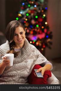 Happy young woman with cup of hot chocolate watching tv