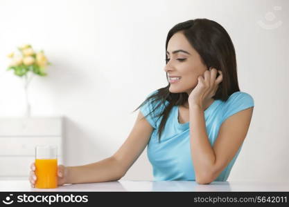 Happy young woman with glass of orange juice at home