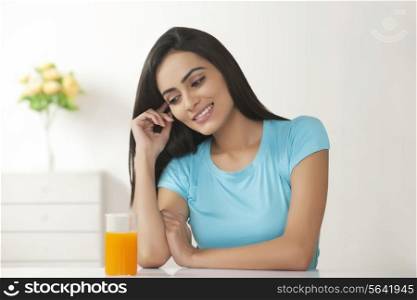 Happy young woman with glass of orange juice at table