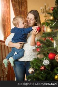 Happy young woman with her baby son decorating Christmas tree