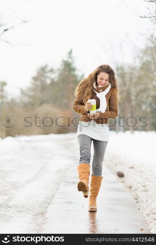 Happy young woman with hot beverage walking in winter park