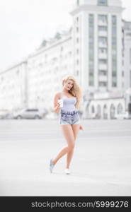 Happy young woman with long curly hair, holding a take away coffee cup and smiling with flirt in front of a camera against urban city traffic background.