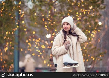 Happy young woman with skates ready to skate on ice rink. Smiling young girl skating on ice rink outdoors