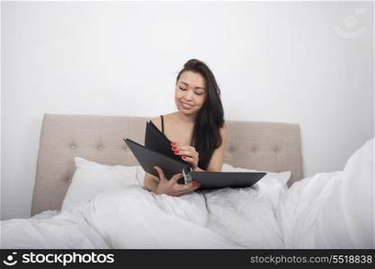 Happy young woman with spiral notepad in bedroom