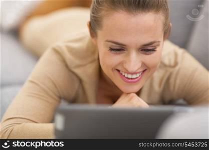 Happy young woman with tablet pc laying on couch