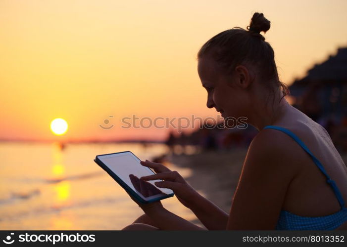 Happy young woman with tablet PC on beach at sunset. Evening sun, sea and beach on background