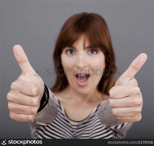 Happy young woman with thumb up over a grey background