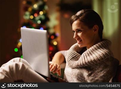 Happy young woman working on laptop in front of christmas tree