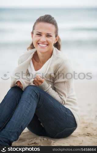 Happy young woman wrapping in sweater while sitting on lonely beach