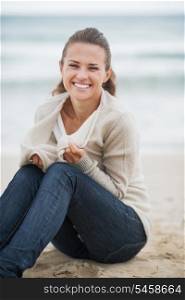 Happy young woman wrapping in sweater while sitting on lonely beach