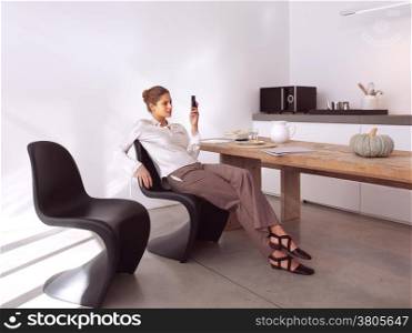 Happy young woman writing a message on her cellphone at home in the kitchen