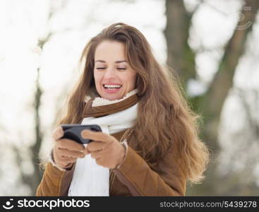 Happy young woman writing sms in winter outdoors