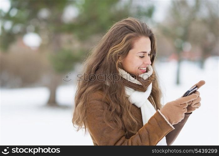 Happy young woman writing sms in winter park