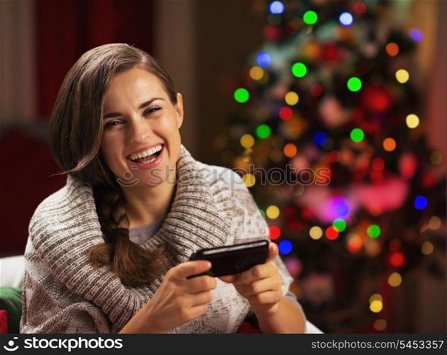 Happy young woman writing sms near christmas tree