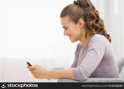Happy young woman writing sms while sitting on divan