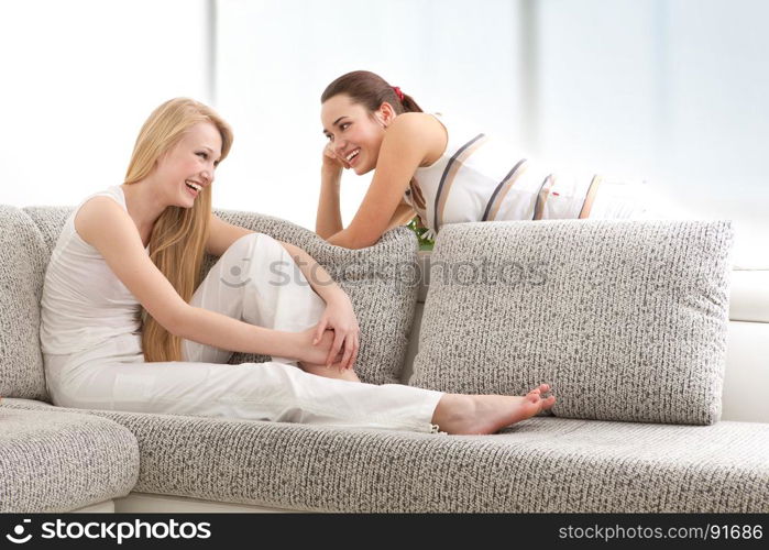 Happy Young Women Chatting, Lying on the Sofa in Living Room