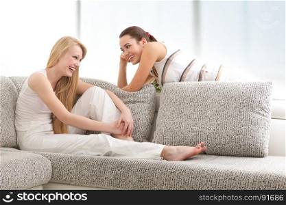Happy Young Women Chatting, Lying on the Sofa in Living Room