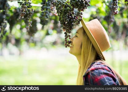 Happy young women gardener holding branches of ripe blue grape