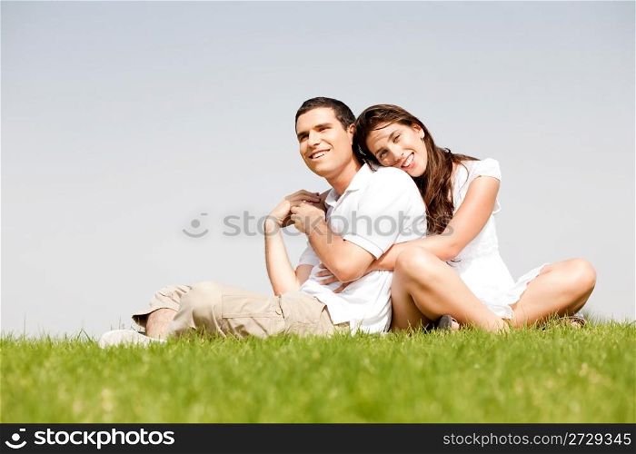 Happy young women with arms around her husband and laying on his shoulder in a park